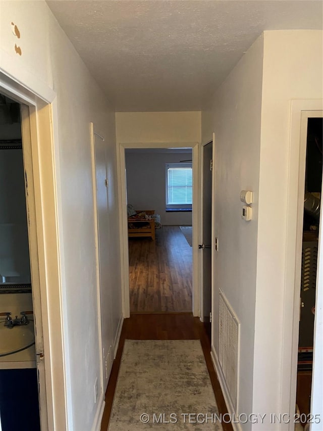 hallway with dark wood-type flooring, sink, and a textured ceiling