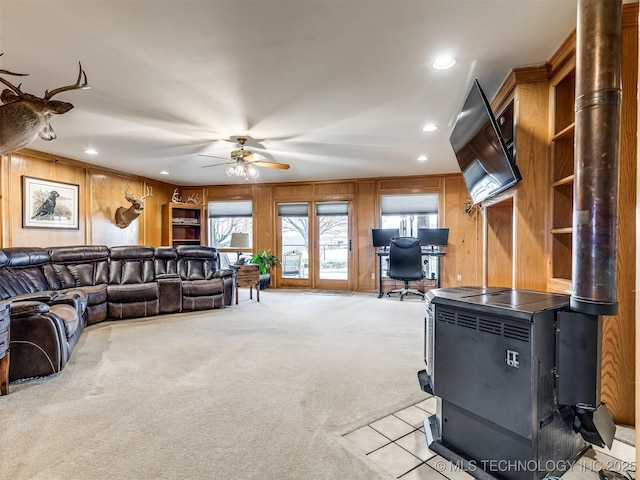 carpeted living room with ceiling fan, a wood stove, and wood walls