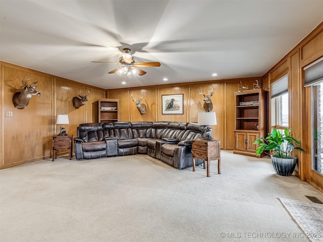 carpeted living room featuring ceiling fan and wood walls