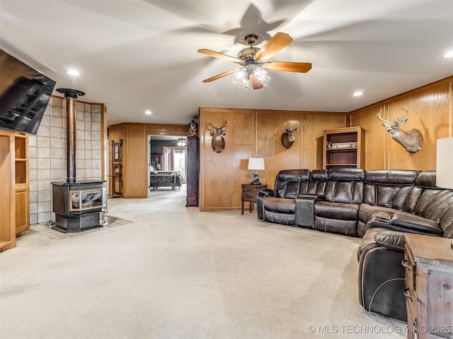 carpeted living room with wood walls, ceiling fan, and a wood stove