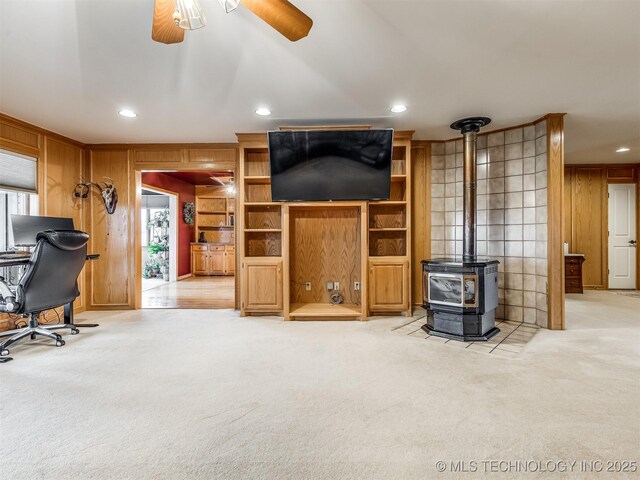 living room featuring wood walls, light carpet, a wood stove, a wealth of natural light, and ceiling fan