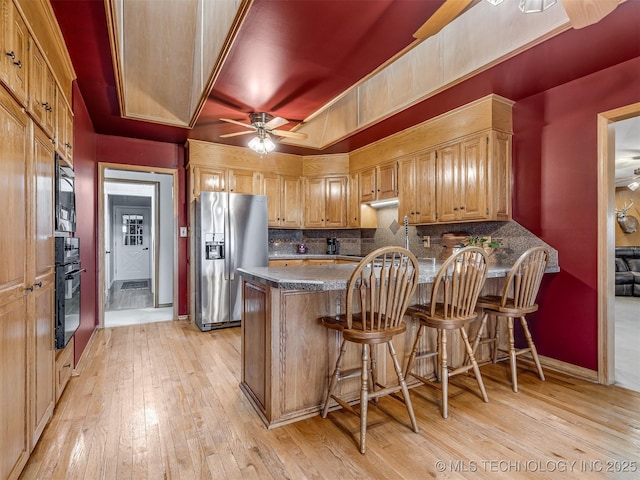 kitchen with light hardwood / wood-style flooring, a breakfast bar area, backsplash, stainless steel appliances, and kitchen peninsula