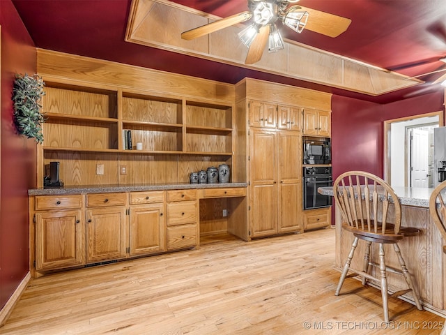 kitchen with light wood finished floors, ceiling fan, brown cabinetry, black appliances, and light stone counters