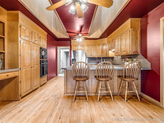 kitchen featuring tasteful backsplash, ceiling fan, a tray ceiling, black appliances, and a peninsula