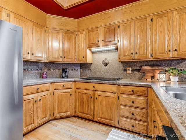 kitchen featuring brown cabinets, black electric stovetop, light wood-style flooring, backsplash, and freestanding refrigerator