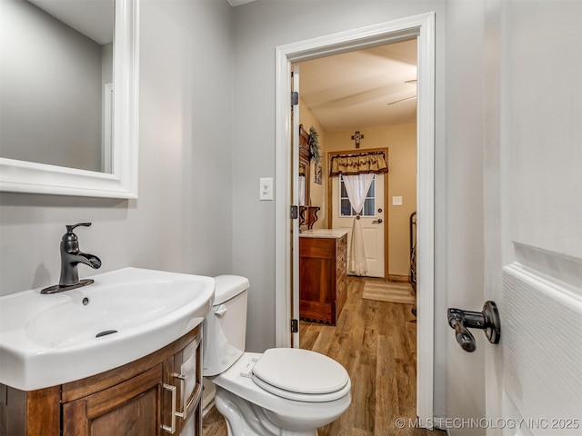 half bathroom featuring wood finished floors, toilet, and vanity