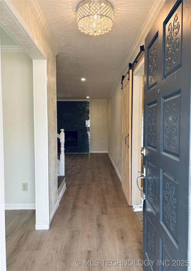 hall with crown molding, wood-type flooring, a textured ceiling, a notable chandelier, and a barn door