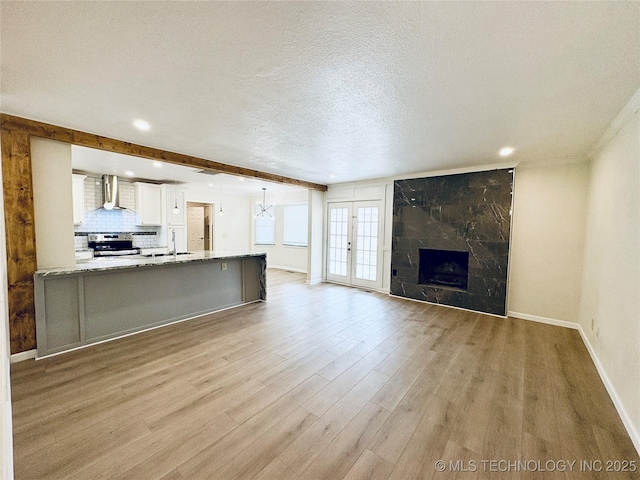 unfurnished living room with sink, beam ceiling, a high end fireplace, a textured ceiling, and light wood-type flooring