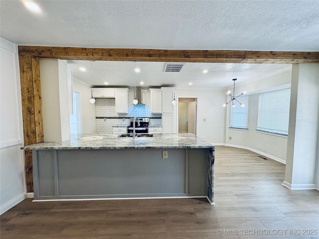 kitchen with pendant lighting, wall chimney range hood, sink, white cabinetry, and light stone countertops