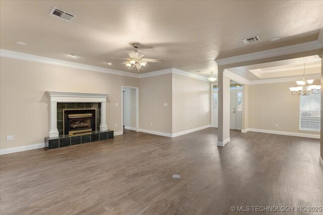 unfurnished living room featuring crown molding, dark hardwood / wood-style floors, a textured ceiling, a tiled fireplace, and ceiling fan with notable chandelier