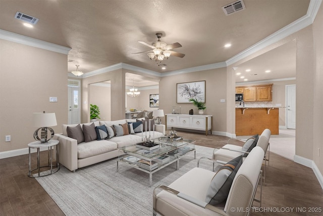 living area featuring ceiling fan with notable chandelier, visible vents, wood finished floors, and baseboards