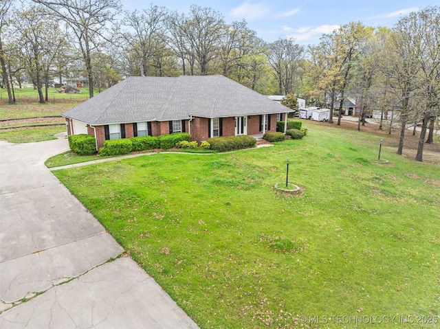 view of front of property with concrete driveway, roof with shingles, an attached garage, a front yard, and brick siding