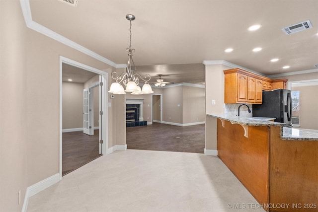 kitchen with black fridge with ice dispenser, visible vents, light stone countertops, and ornamental molding
