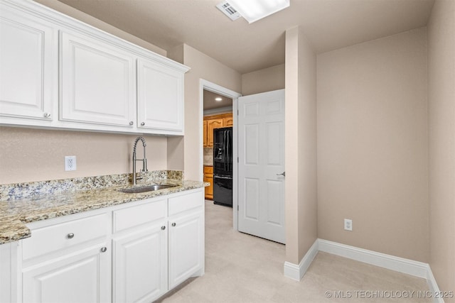 kitchen featuring black refrigerator with ice dispenser, baseboards, white cabinetry, and a sink