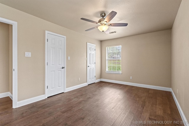 unfurnished bedroom featuring baseboards, dark wood-style flooring, ceiling fan, and visible vents