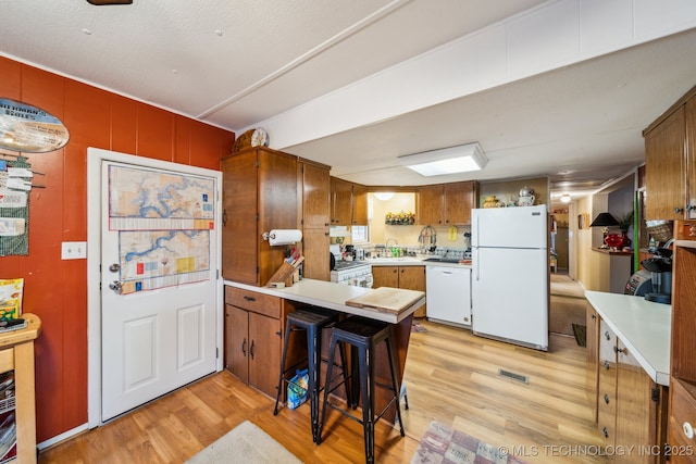 kitchen featuring sink, a breakfast bar area, white appliances, and light hardwood / wood-style flooring