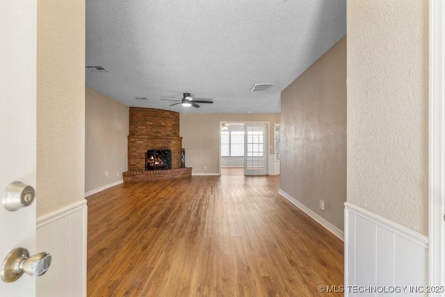 unfurnished living room with ceiling fan, a brick fireplace, hardwood / wood-style floors, and a textured ceiling