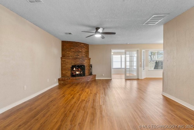 unfurnished living room with ceiling fan, a fireplace, hardwood / wood-style floors, and a textured ceiling