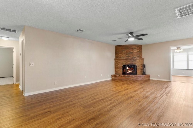 unfurnished living room with ceiling fan, a fireplace, hardwood / wood-style floors, and a textured ceiling