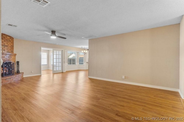 unfurnished living room featuring light hardwood / wood-style flooring, ceiling fan with notable chandelier, a fireplace, and a textured ceiling