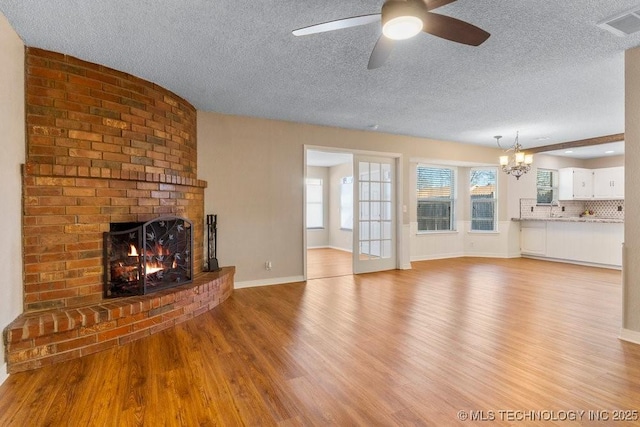 unfurnished living room with a brick fireplace, ceiling fan with notable chandelier, a textured ceiling, and light wood-type flooring