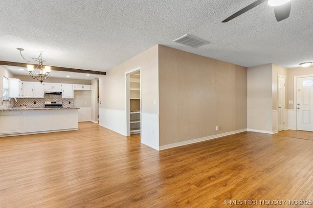 unfurnished living room featuring sink, ceiling fan with notable chandelier, a textured ceiling, and light hardwood / wood-style flooring