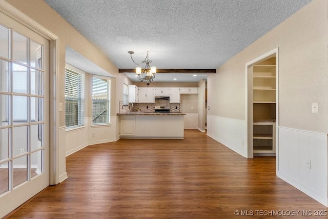 unfurnished living room with an inviting chandelier, dark wood-type flooring, a textured ceiling, and beamed ceiling