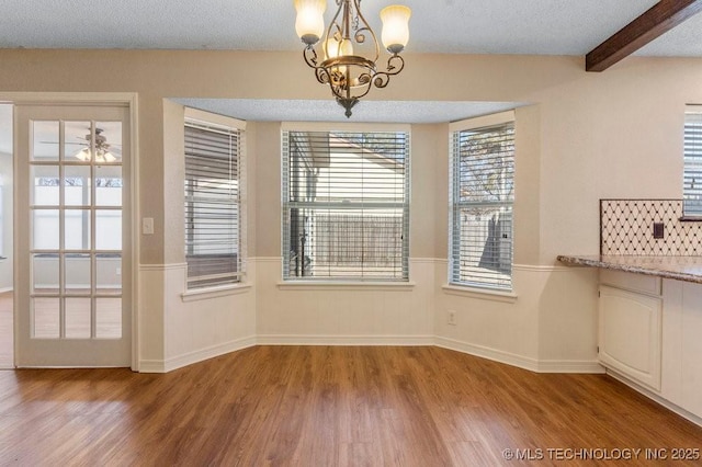 unfurnished dining area featuring beamed ceiling, wood-type flooring, a notable chandelier, and a textured ceiling