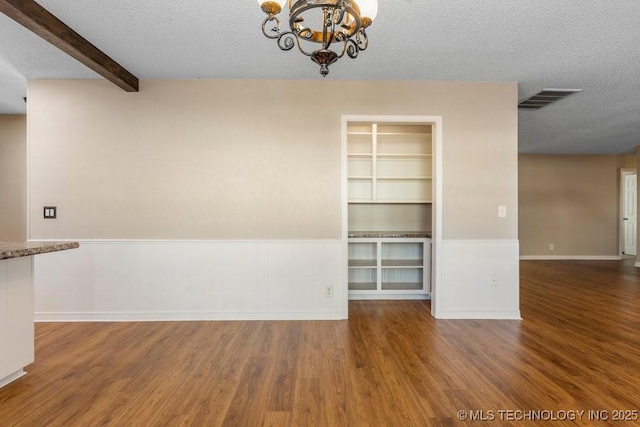 spare room featuring a textured ceiling, dark hardwood / wood-style floors, built in features, a notable chandelier, and beam ceiling