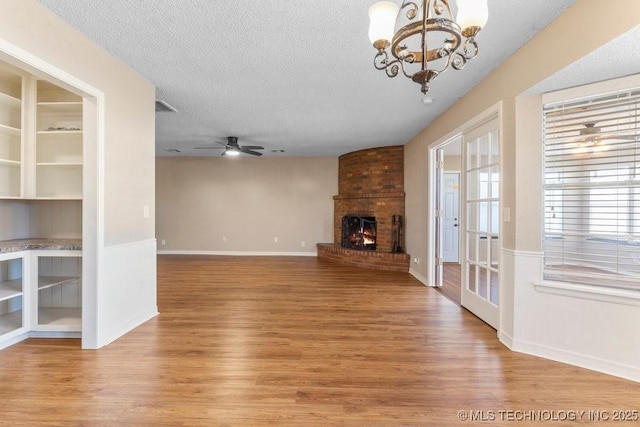 unfurnished living room featuring a brick fireplace, ceiling fan with notable chandelier, light hardwood / wood-style flooring, and a textured ceiling