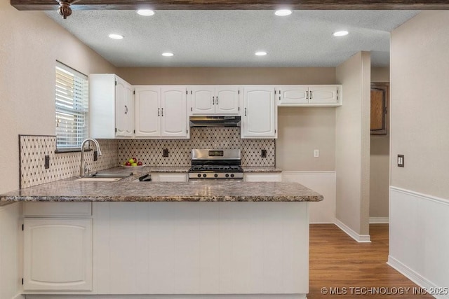 kitchen with stainless steel range oven, sink, white cabinetry, light stone counters, and kitchen peninsula