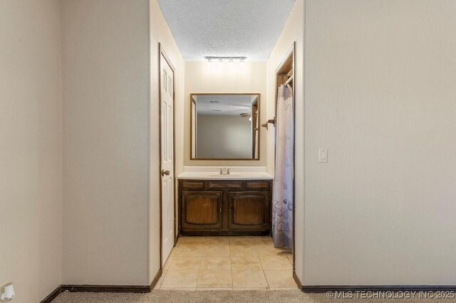 corridor with light carpet, rail lighting, sink, and a textured ceiling