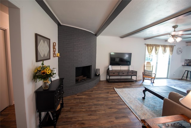 living room with ceiling fan, dark hardwood / wood-style floors, beam ceiling, and a brick fireplace