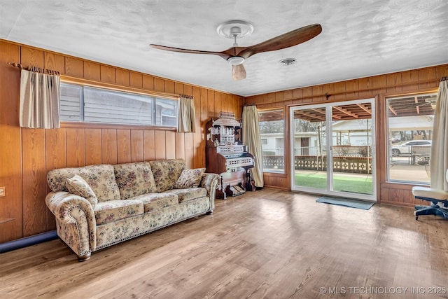 sitting room featuring ceiling fan, wood walls, light hardwood / wood-style flooring, and a wealth of natural light