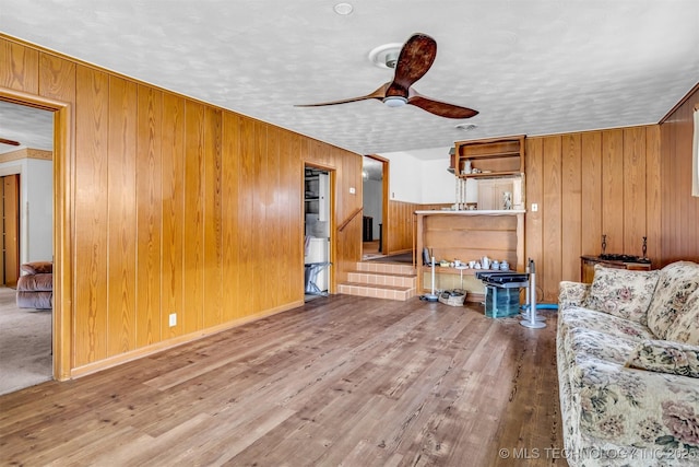 living room with ceiling fan, wood-type flooring, and wood walls