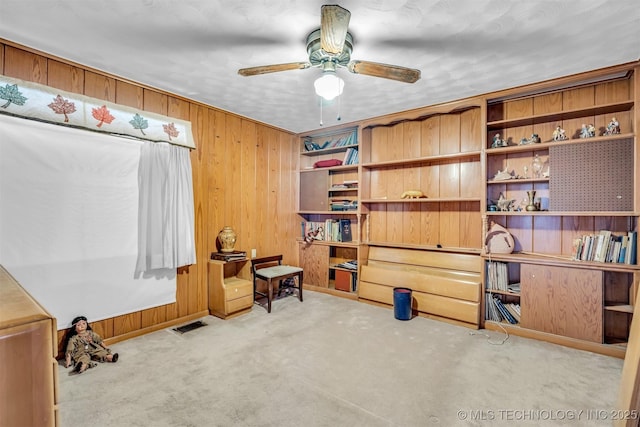 misc room featuring ceiling fan, light colored carpet, and wood walls