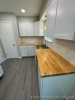 kitchen with dark hardwood / wood-style floors, wood counters, tasteful backsplash, white cabinetry, and sink