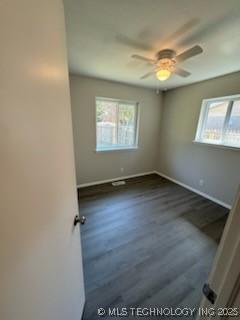 empty room featuring ceiling fan, a healthy amount of sunlight, and dark hardwood / wood-style floors