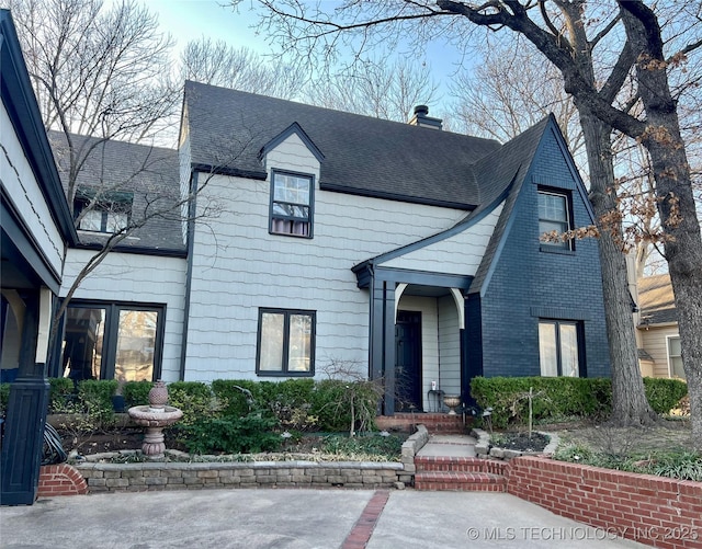 view of front facade featuring brick siding, a chimney, and roof with shingles