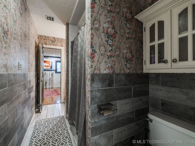 8918 S Lakewood Ave, Tulsa, OK 74137 - bathroom with wallpapered walls, tile walls, curtained shower, and a wainscoted wall