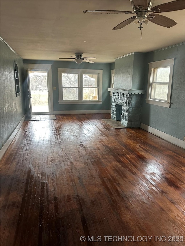 unfurnished living room featuring a stone fireplace, dark hardwood / wood-style floors, and ceiling fan