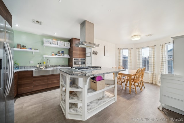 kitchen with appliances with stainless steel finishes, island range hood, sink, a center island, and light hardwood / wood-style floors