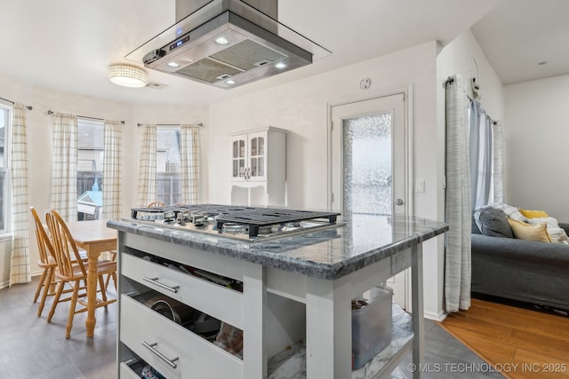 kitchen featuring island range hood, dark hardwood / wood-style flooring, stainless steel gas cooktop, and dark stone counters