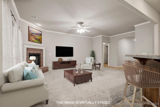 living room featuring ornamental molding, carpet flooring, ceiling fan, and a fireplace