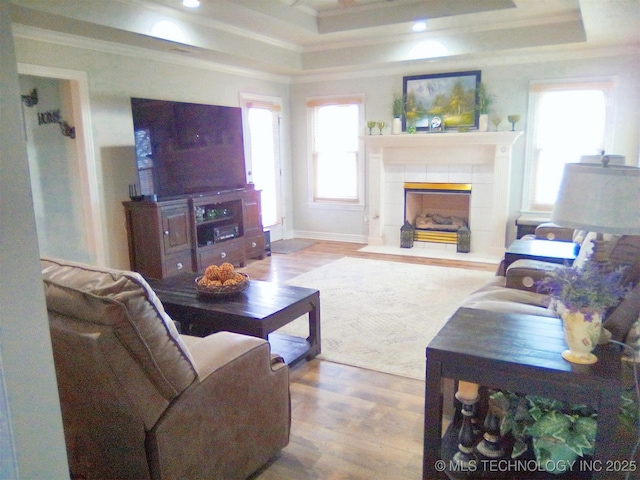 living room with a tile fireplace, ornamental molding, a raised ceiling, and hardwood / wood-style floors