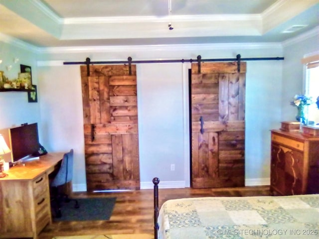 bedroom with ornamental molding, a barn door, hardwood / wood-style floors, and a tray ceiling