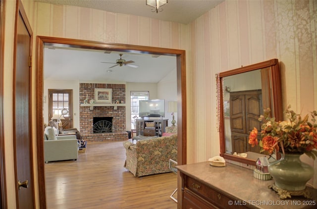 living room with ceiling fan, lofted ceiling, a fireplace, and light hardwood / wood-style flooring