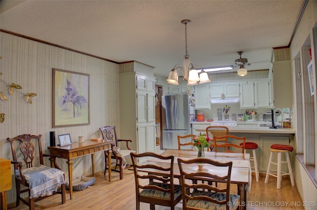 dining space with ornamental molding, sink, a textured ceiling, and light wood-type flooring