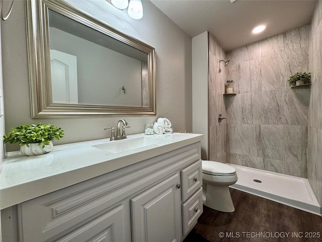 bathroom with vanity, toilet, wood-type flooring, and a tile shower