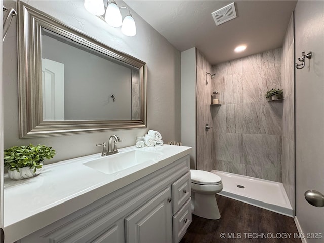 bathroom featuring hardwood / wood-style flooring, vanity, toilet, and a tile shower